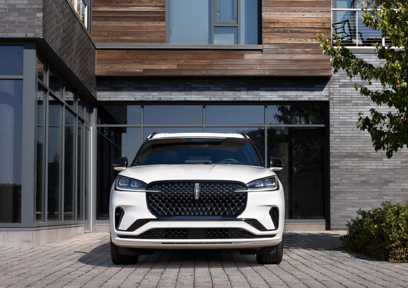 A white 2025 Lincoln Aviator® SUV is shown parked outside a modern building with gray brick and wood accents. | Astro Lincoln in Pensacola FL