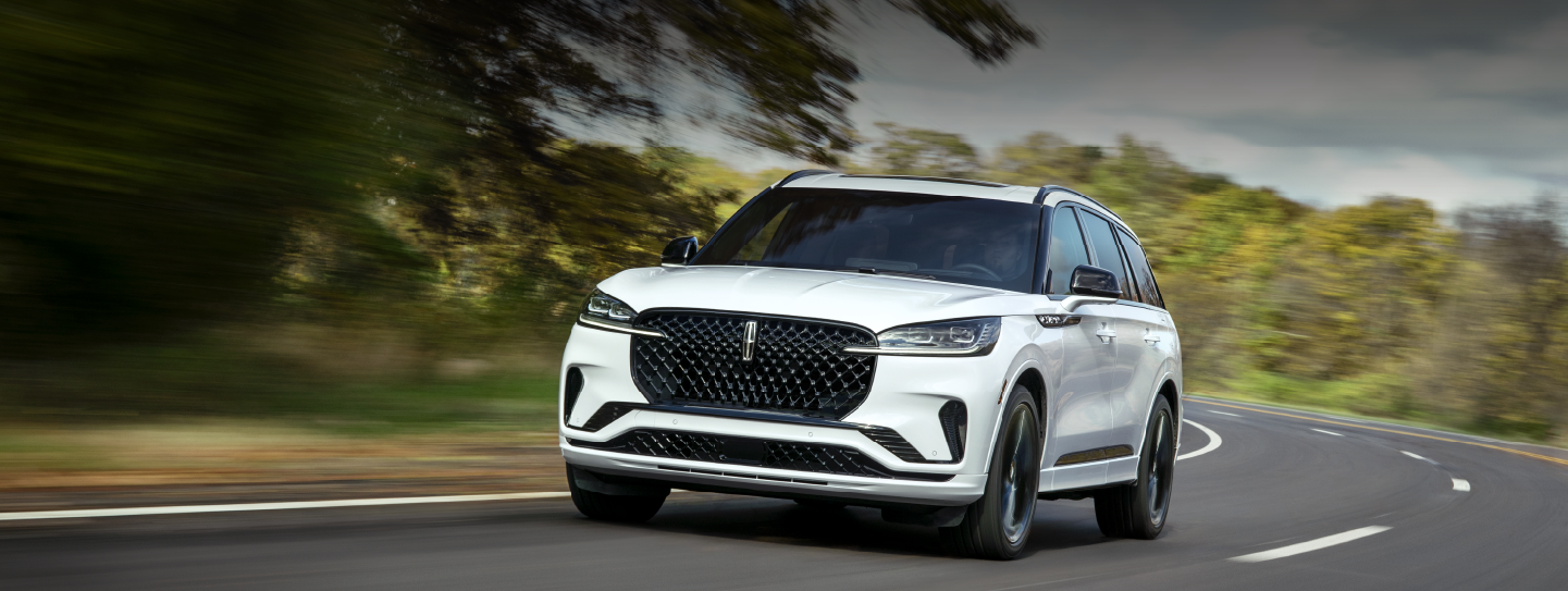 A white 2025 Lincoln Aviator® SUV is being driven down a road lined with trees. | Astro Lincoln in Pensacola FL