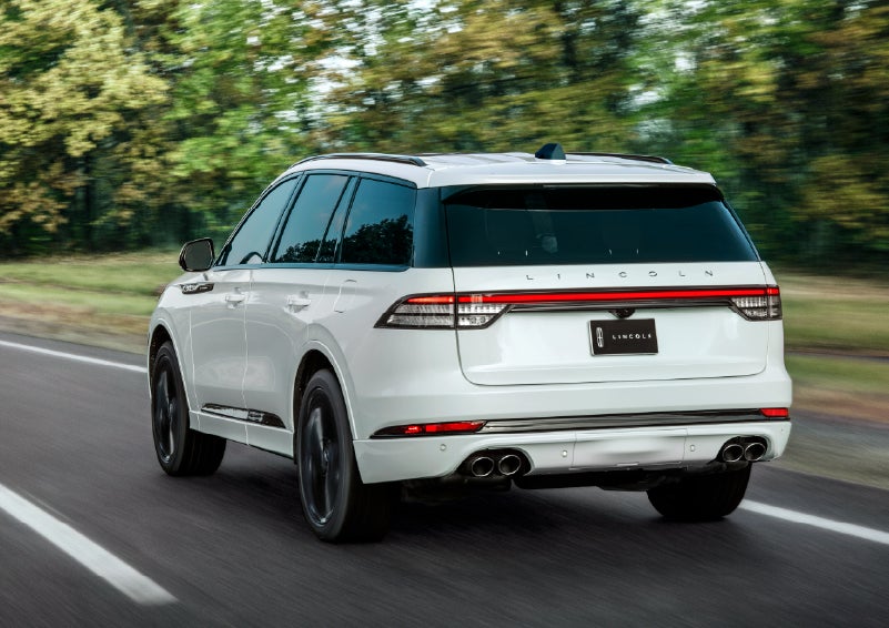 A white 2026 Lincoln Aviator® SUV is being driven away down a road lined with colorful trees. | Astro Lincoln in Pensacola FL