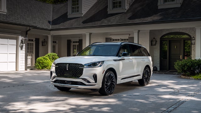 A white 2026 Lincoln Aviator® SUV is parked in the driveway of a luxury home. | Astro Lincoln in Pensacola FL