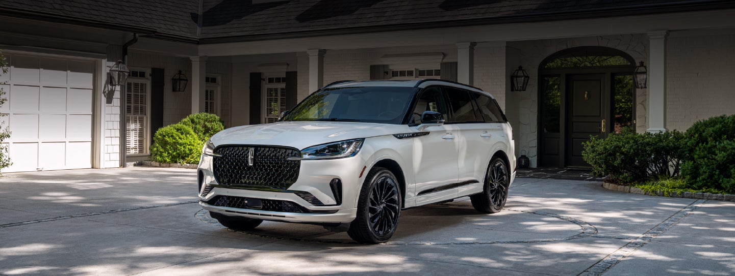 A white 2026 Lincoln Aviator® SUV is parked in the driveway of a luxury home. | Astro Lincoln in Pensacola FL