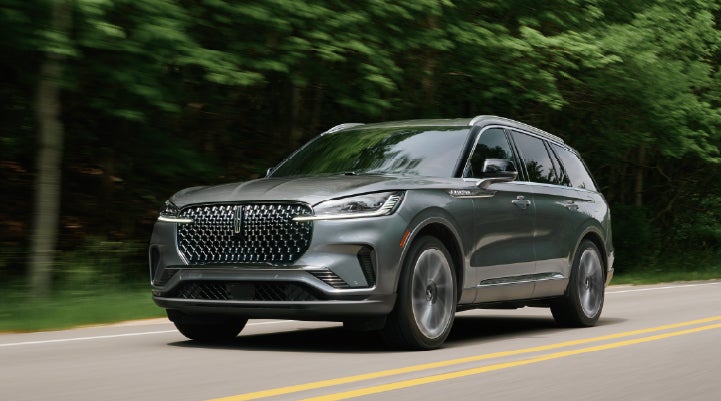 A 2027 Lincoln Aviator® SUV is being driven down a road lined with trees. | Astro Lincoln in Pensacola FL